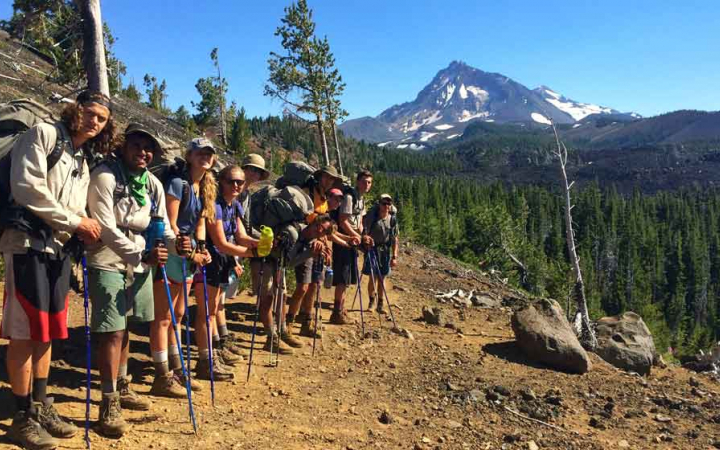 a group of teens pose with a mountain on backpacking trip